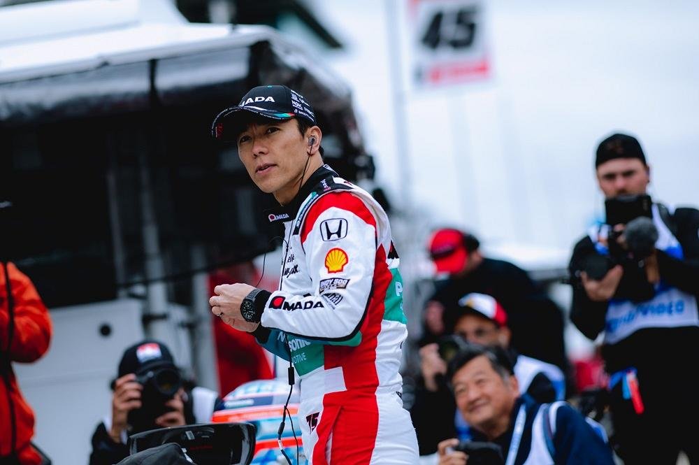 A man stands in a car racing suit.