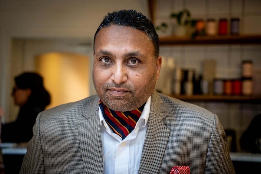 Lucky Singh Saini sits at a table in a restaurant and smiles