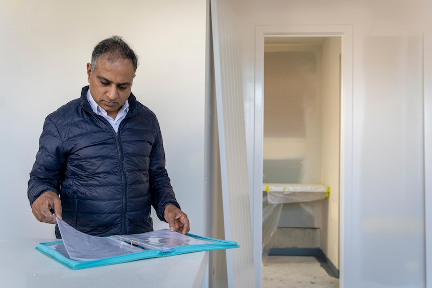 Surya Kant stands in a kitchen under construction and reads paperwork.