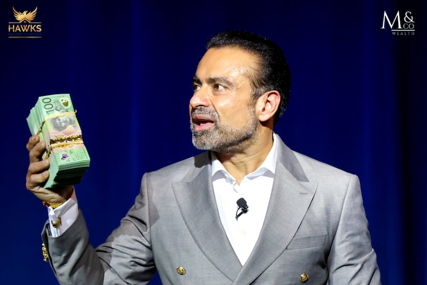 A man holding a huge wad of hundred dollar notes while giving a speech.