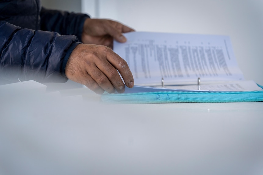 Surya Kant's hands hold printed documents against a white kitchen bench.