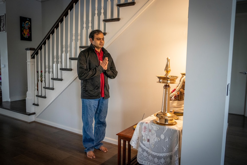 A man standing in a prayer position at a small prayer table.