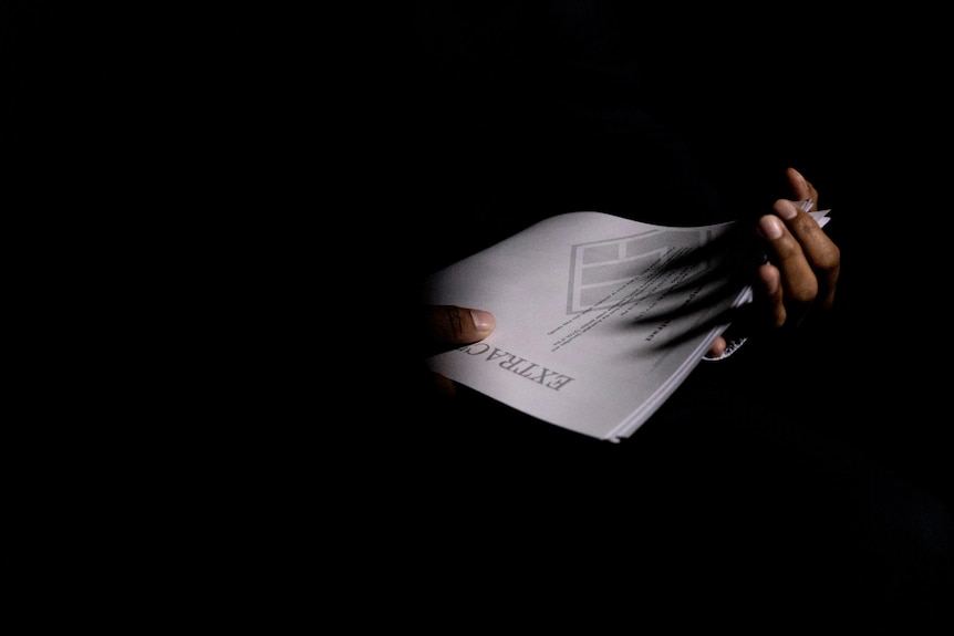 Two hands holding documents in a dark room.  