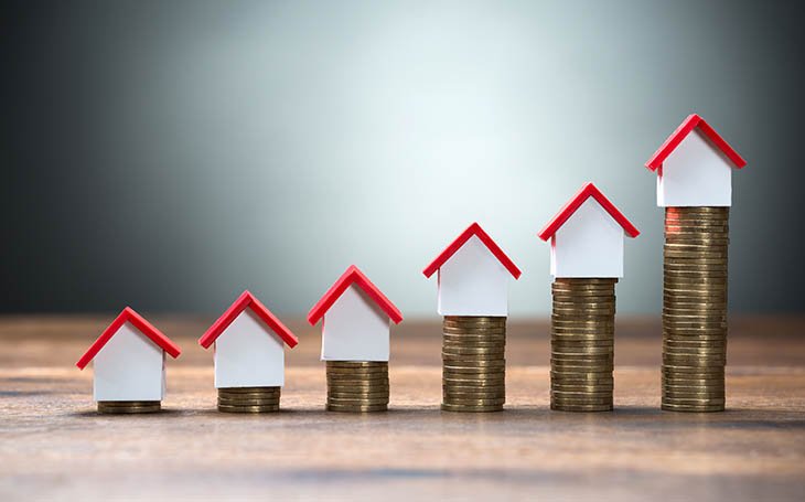 House models arranged on stacked coins at table against gray background asking gprices